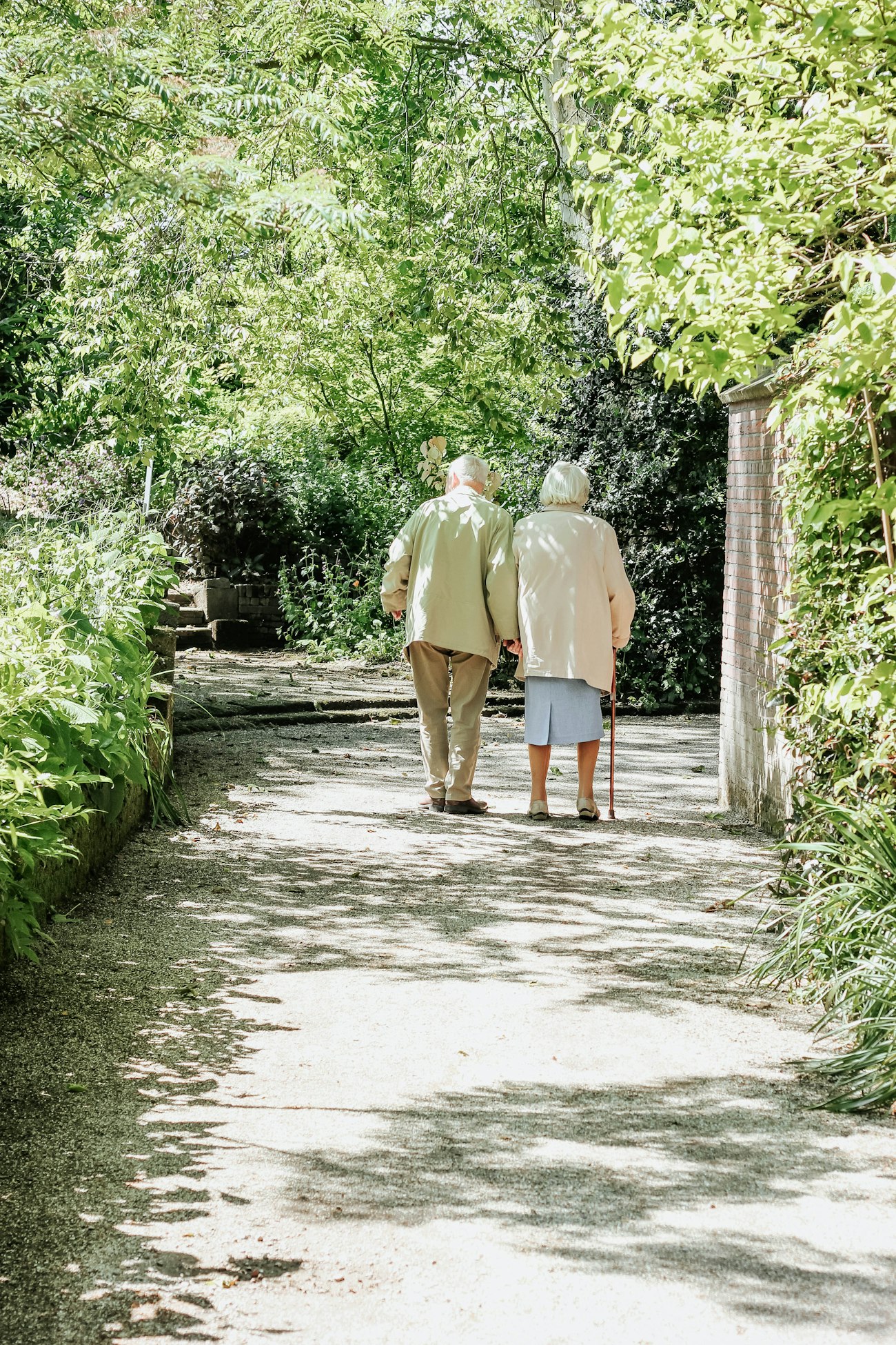 An older couple walking together along a sunlit garden path